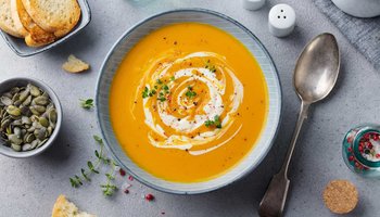 Cremige Kürbissuppe mit Sahne und frischen Kräutern garniert