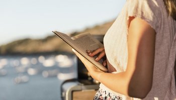 Das Foto zeigt eine Frau, die am Ufer eines Sees ein Buch liest.