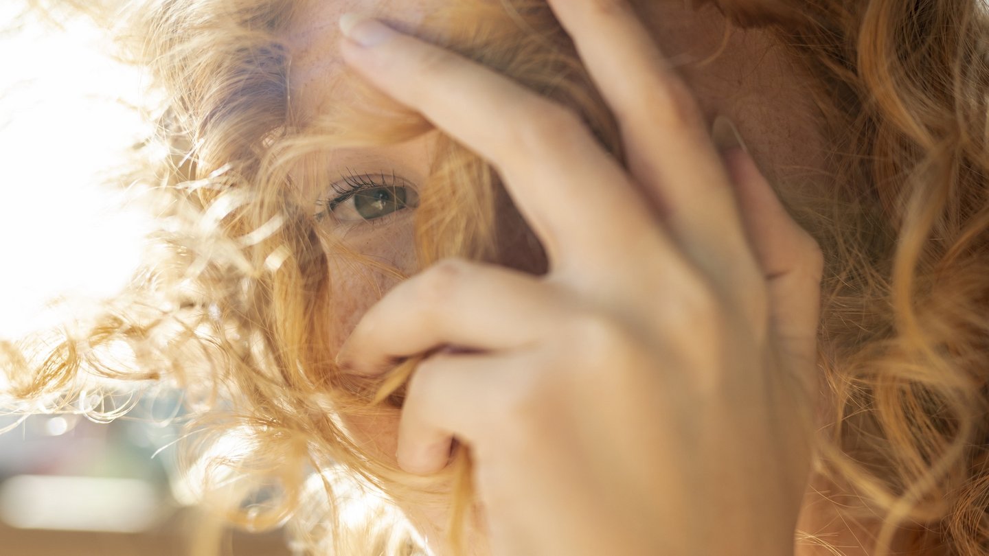 Das Foto zeigt eine Frau in der Sonne, die Ihr Auge mit der Hand bedeckt.