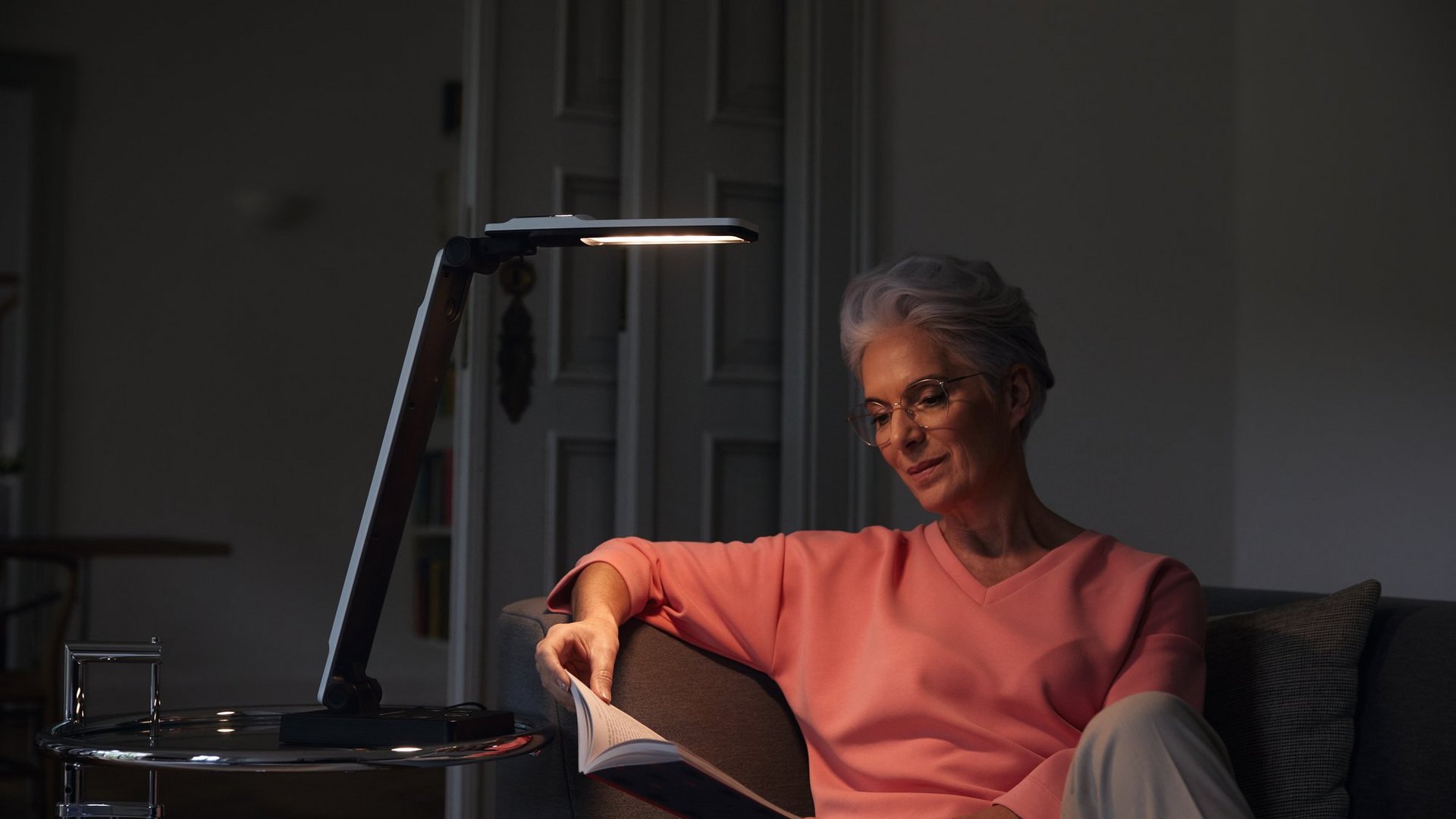 Das Foto zeigt eine Frau, die mit elumentis LED im Dämmerlicht ein Buch auf dem Sofa liest.