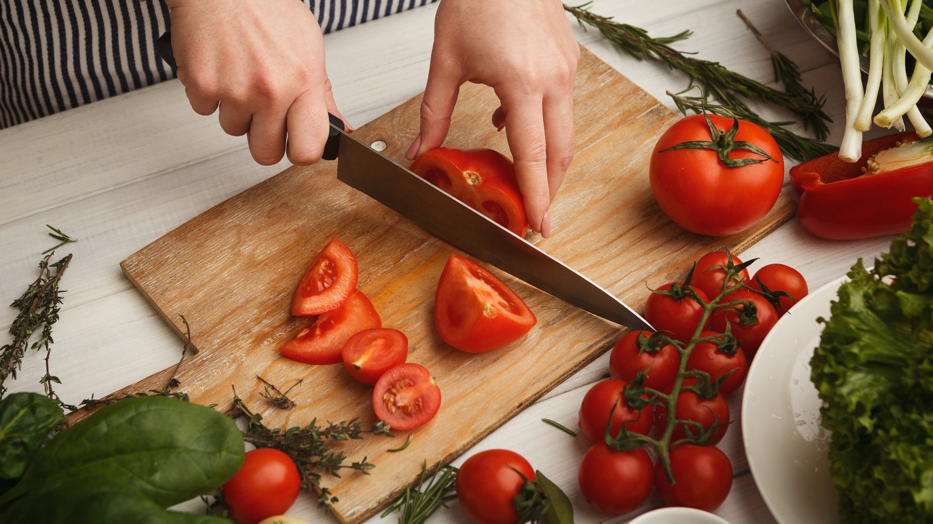 Das Foto zeigt die Draufsicht einer Frau, die Tomaten auf einem Schneidebrett schneidet.