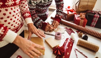 Das Foto zeigt zwei Personen, die Geschenke für Weihnachten einpacken.