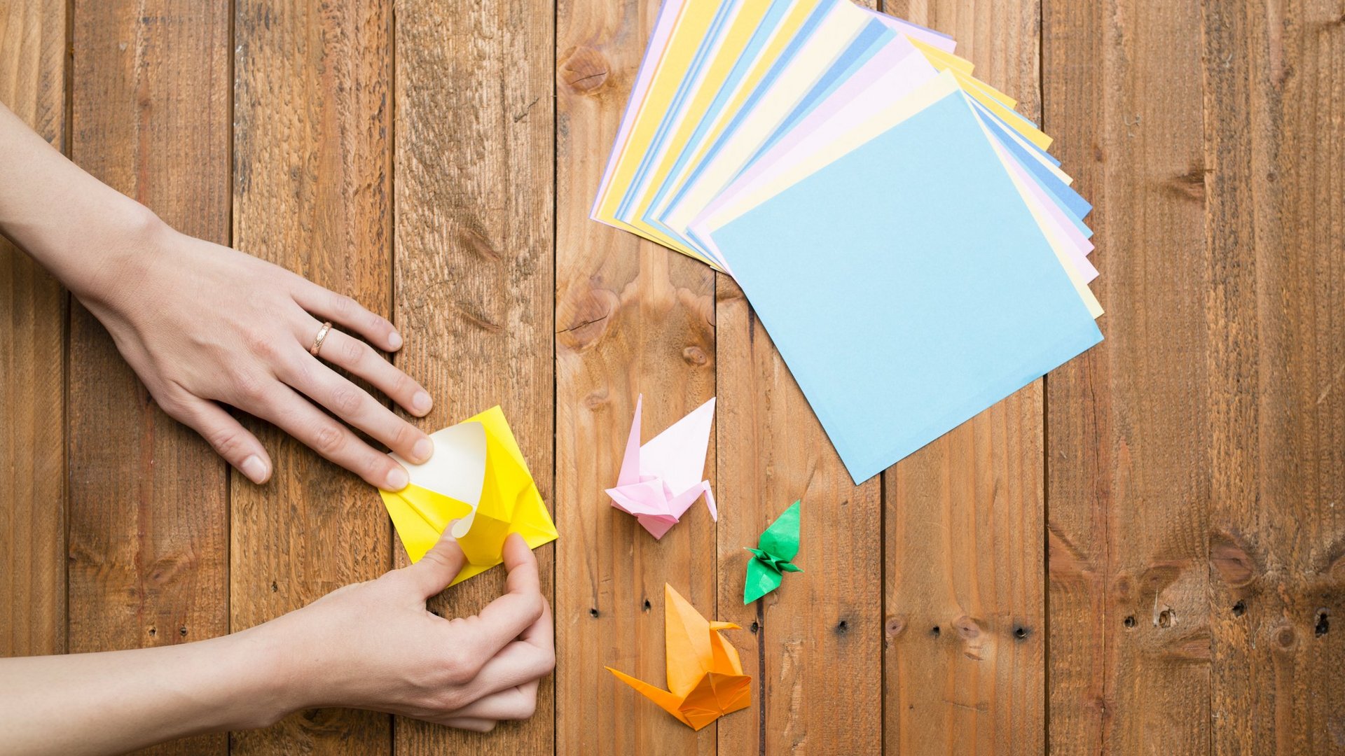 Das Foto zeigt die Hände einer Person, die bunte Origami Figuren faltet.