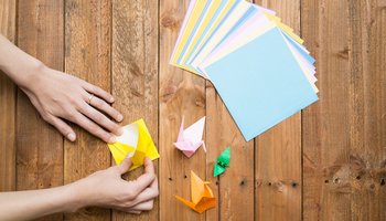 Das Foto zeigt die Hände einer Person, die bunte Origami Figuren faltet.