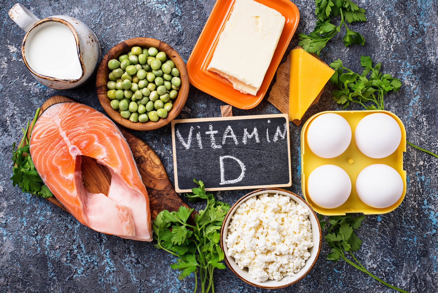 Das Foto zeigt gesunde Lebensmittel und eine Tafel, auf der “Vitamin D” geschrieben steht.