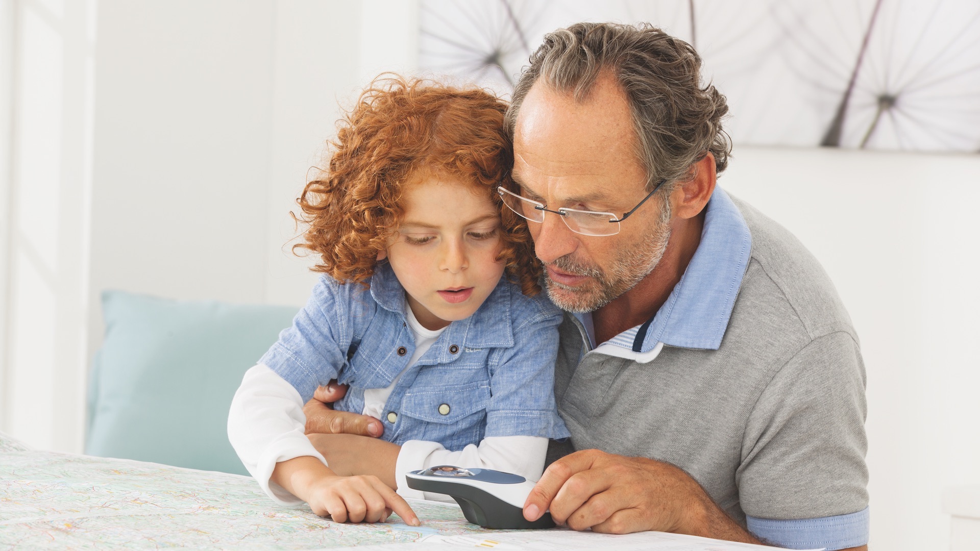 Das Bild zeigt einen älteren Herrn, der gemeinsam mit einem Kind mit der Leuchtlupe eine Landkarte liest.